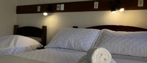 A hotel room with a bed, two pillows, a rolled-up towel, and two framed pictures on the wall.