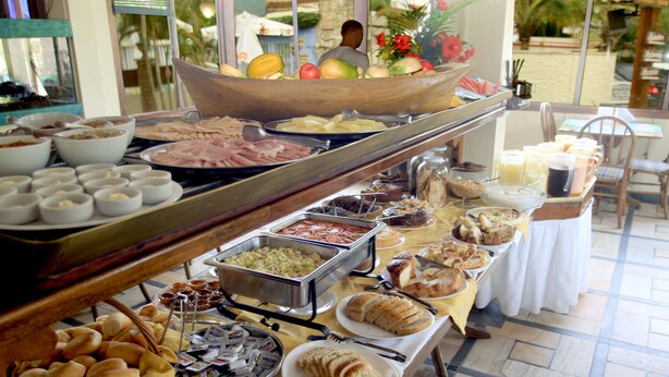 Un bufé con diferentes opciones de comida, incluyendo frutas, carnes y pasteles.