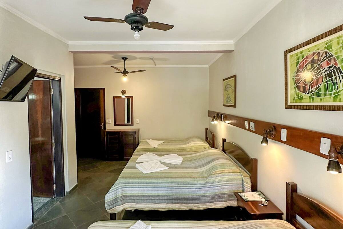 Ein Hotelzimmer mit zwei Betten, einem Deckenventilator, einem Schreibtisch und einem Gemälde an der Wand.