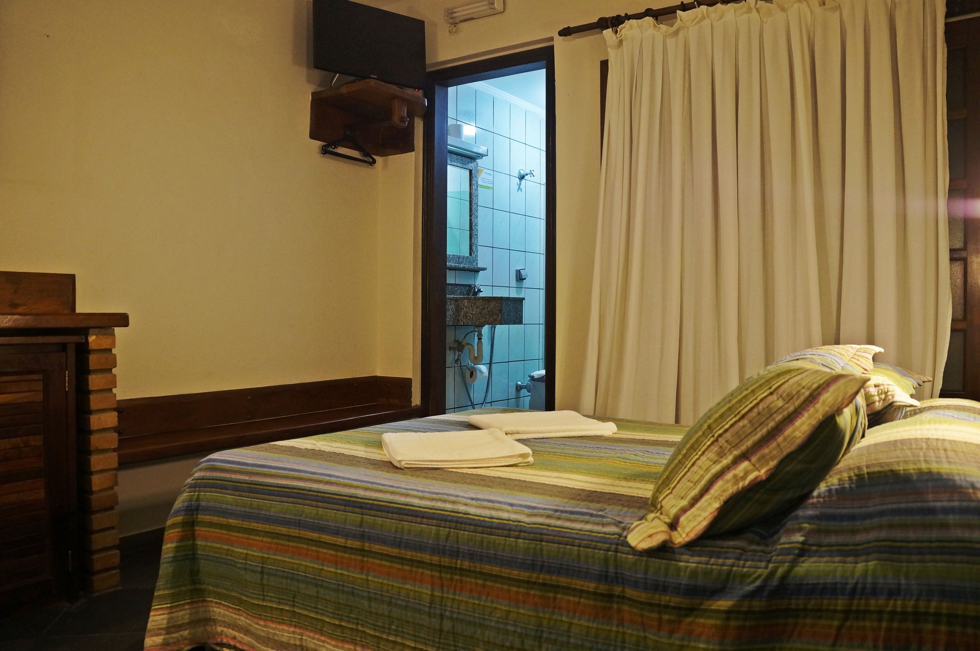 Habitación de hotel con cama, cabecero de madera, baño visible a través de una puerta abierta y una cortina.