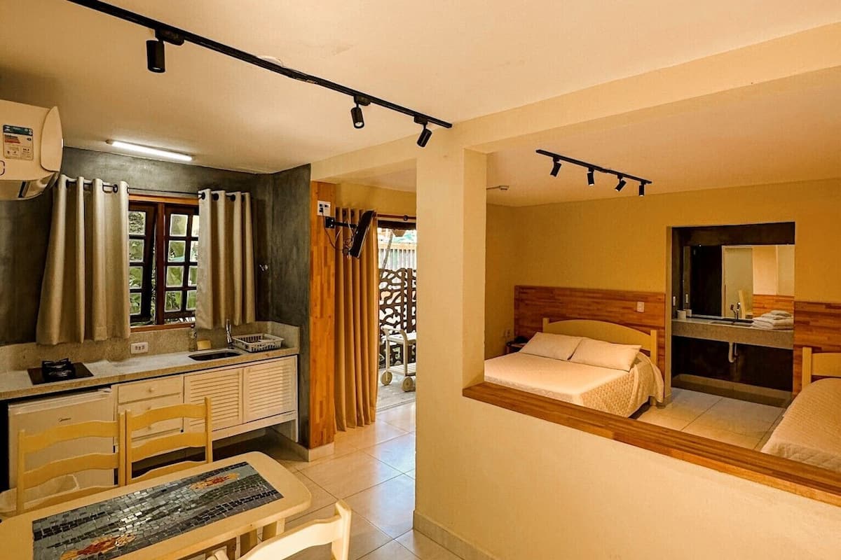 Ein kompaktes Hotelzimmer mit Küchenzeile, einem Essbereich mit einem Mosaik-Tisch und einem Bett mit Holz Kopfteil.
