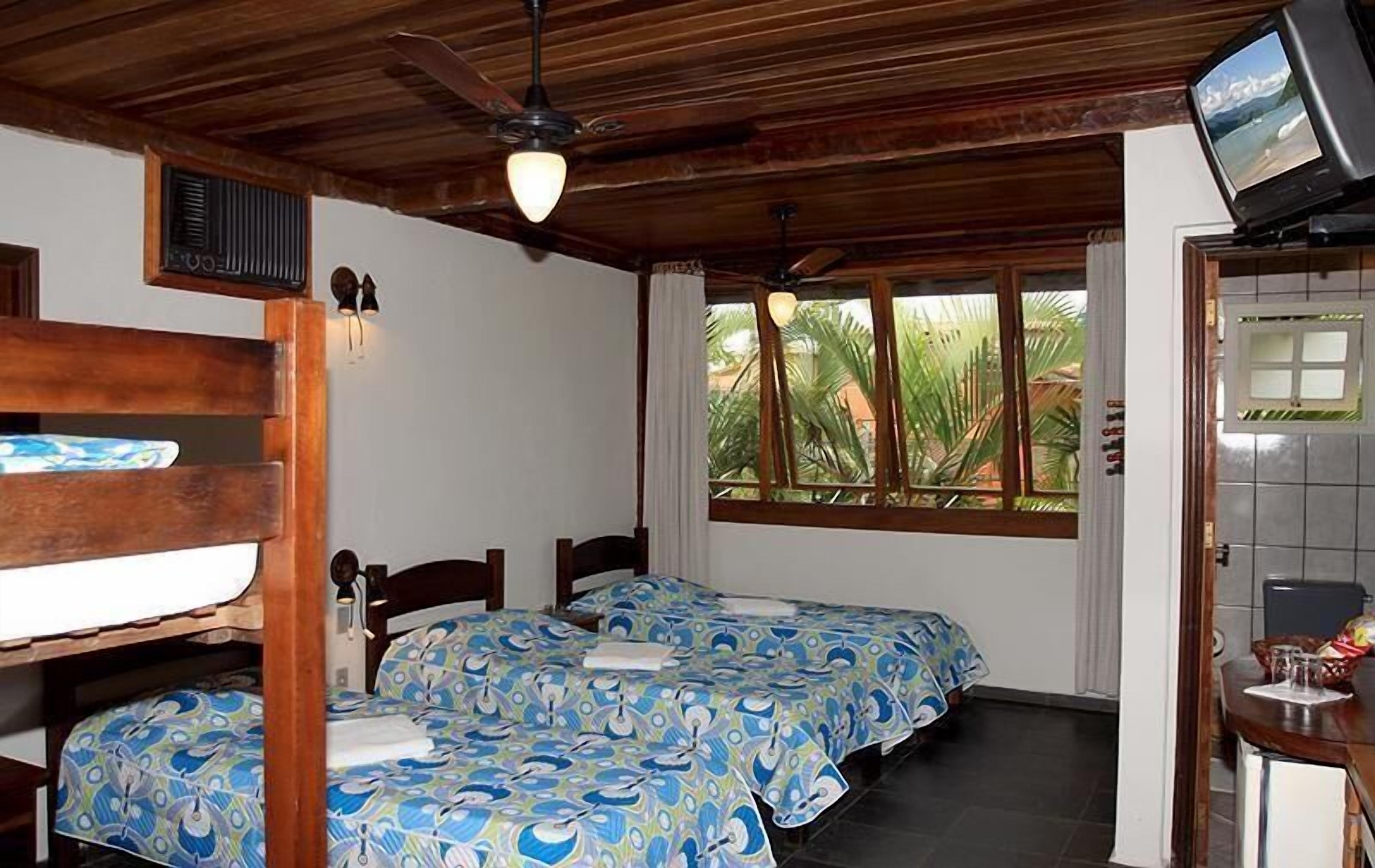 Una habitación con dos camas, ventilador de techo, televisión y ventana con vistas a zonas verdes.