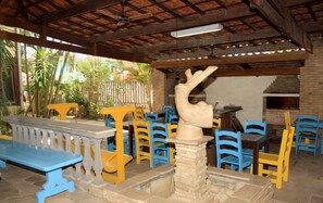 Un patio al aire libre con suelo de piedra, mesas y sillas de madera en azul y amarillo.