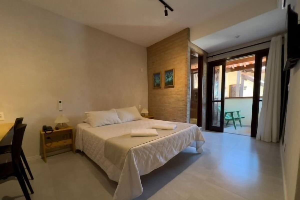 Ein Schlafzimmer mit Bett, Schreibtisch und Stuhl. Ein Fenster und eine Tür führen in einen Außenbereich.