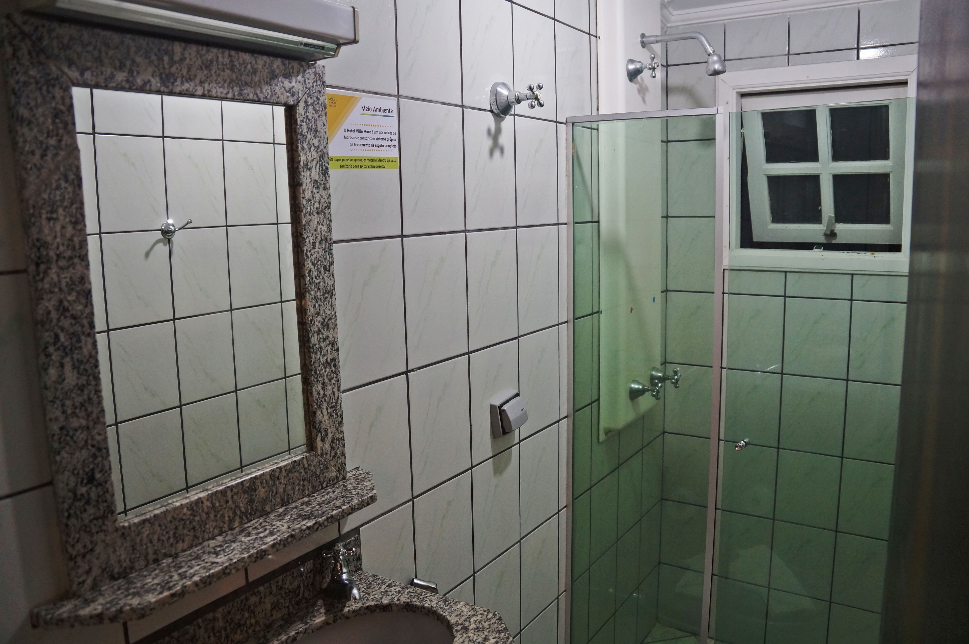 A bathroom with a granite countertop, a mirror, a green-tiled shower enclosure, and a window.
