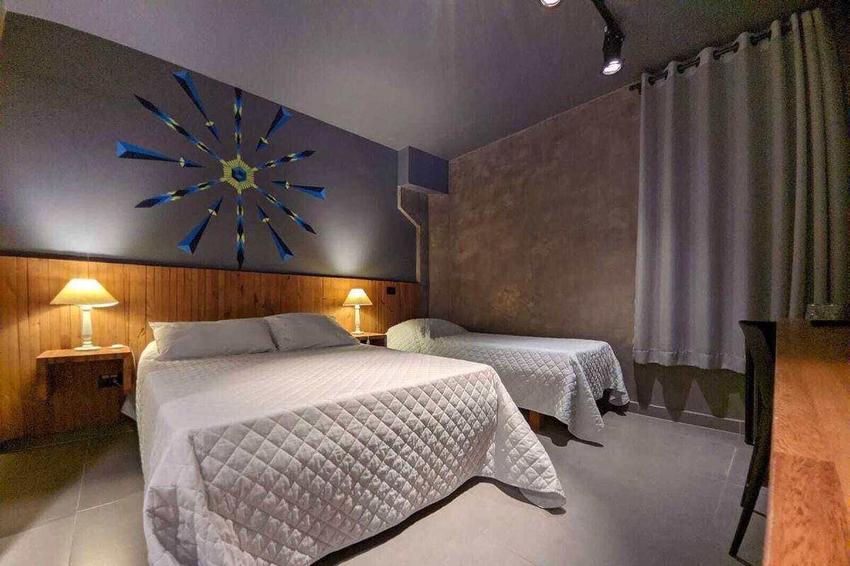 Ein Hotelzimmer mit zwei Betten, einem modernen Wandbild und einem großen Fenster mit Vorhängen.