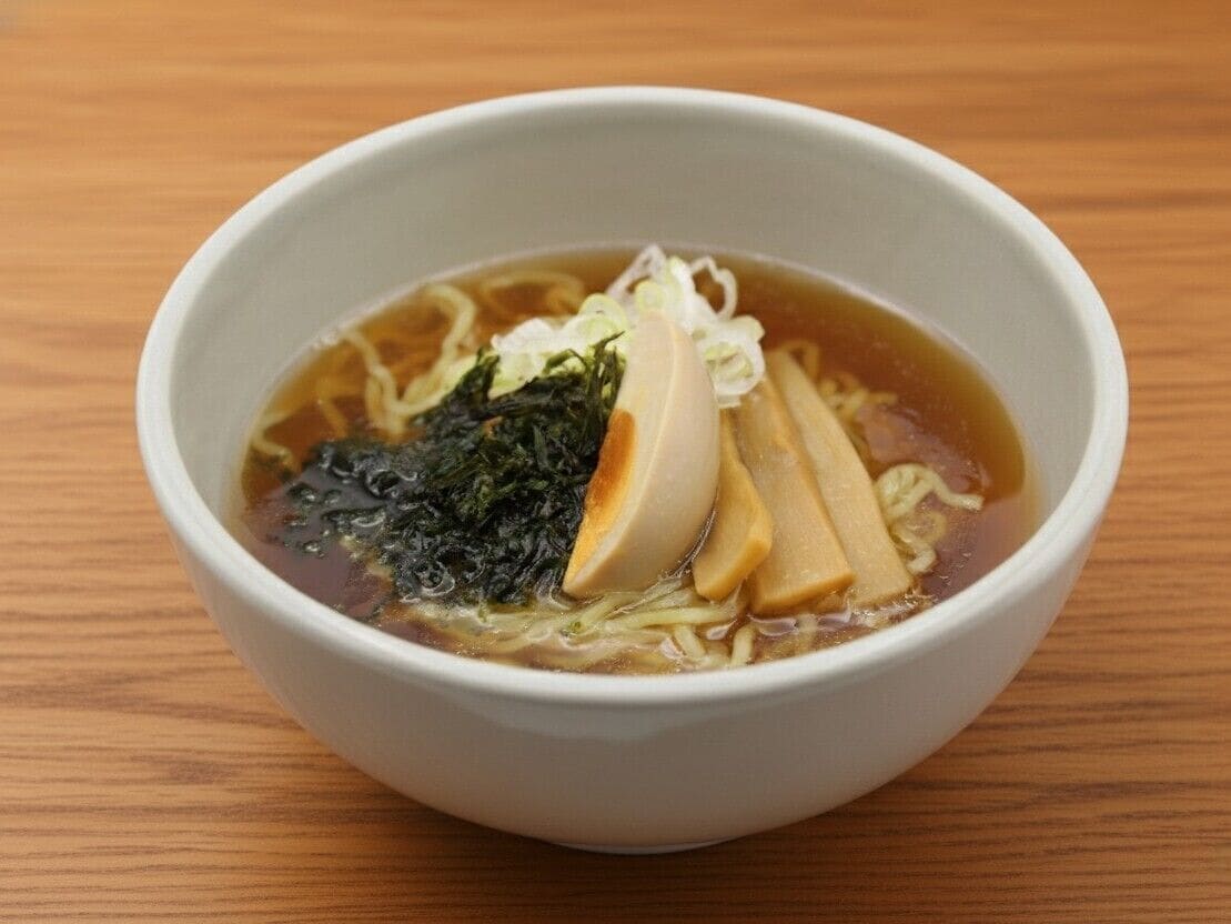 Eine Schüssel Ramen mit Nudeln, Algen und geschnittenem Fleisch auf einem Holztisch.
