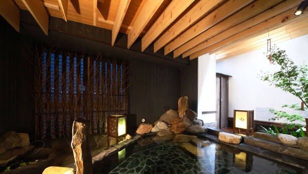 Ett traditionellt japanskt onsen-bad med en varm källa omgiven av sten, träbjälkar och ett bambustaket.