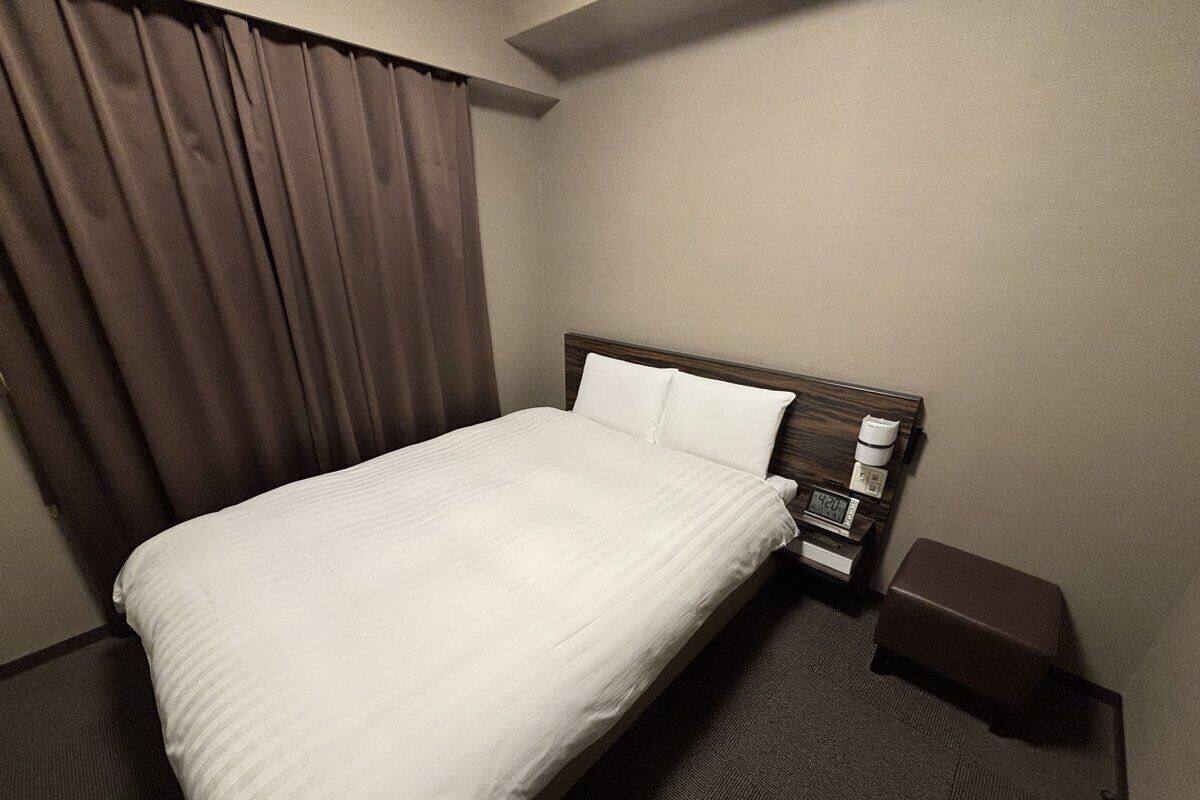 Una habitación de hotel con una cama individual, una mesita de noche, una lámpara y una pequeña mesa con cafetera.