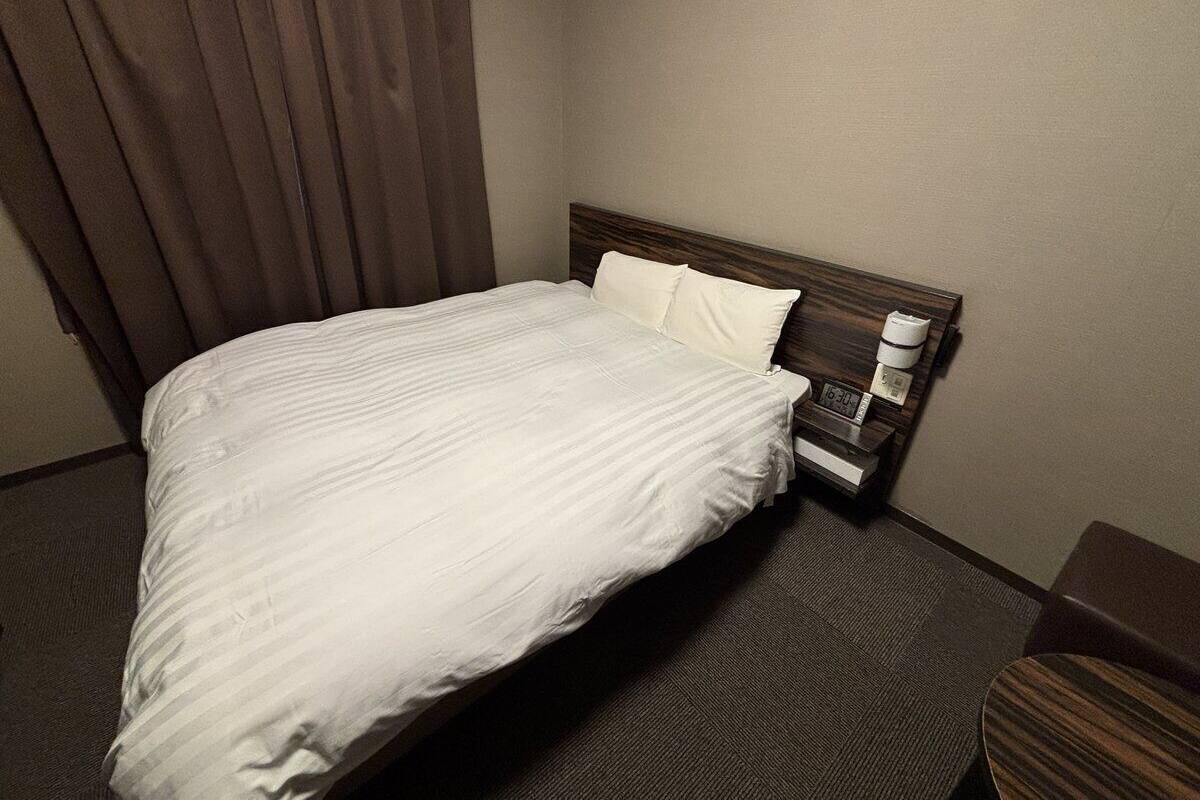 Ein Hotelzimmer mit einem Bett, einem Nachttisch, einer Uhr und einem Vorhang.