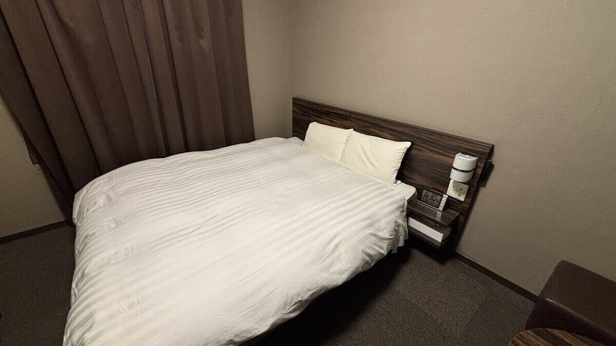 Ein Hotelzimmer mit einem Bett, einem Nachttisch, einer Lampe und einem Fenster mit Vorhängen.