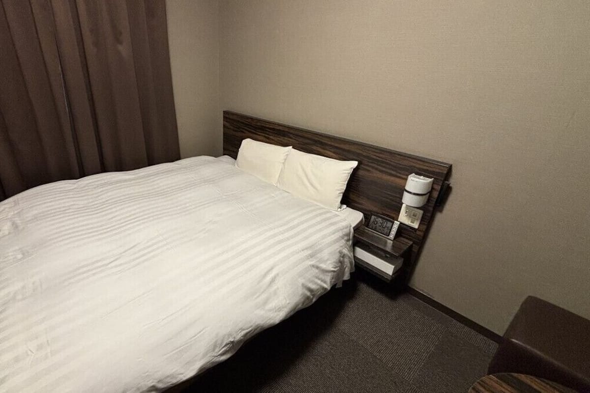 Ein Hotelzimmer mit einem Bett, einem Nachttisch, einer Lampe und einem Fenster mit Vorhängen.