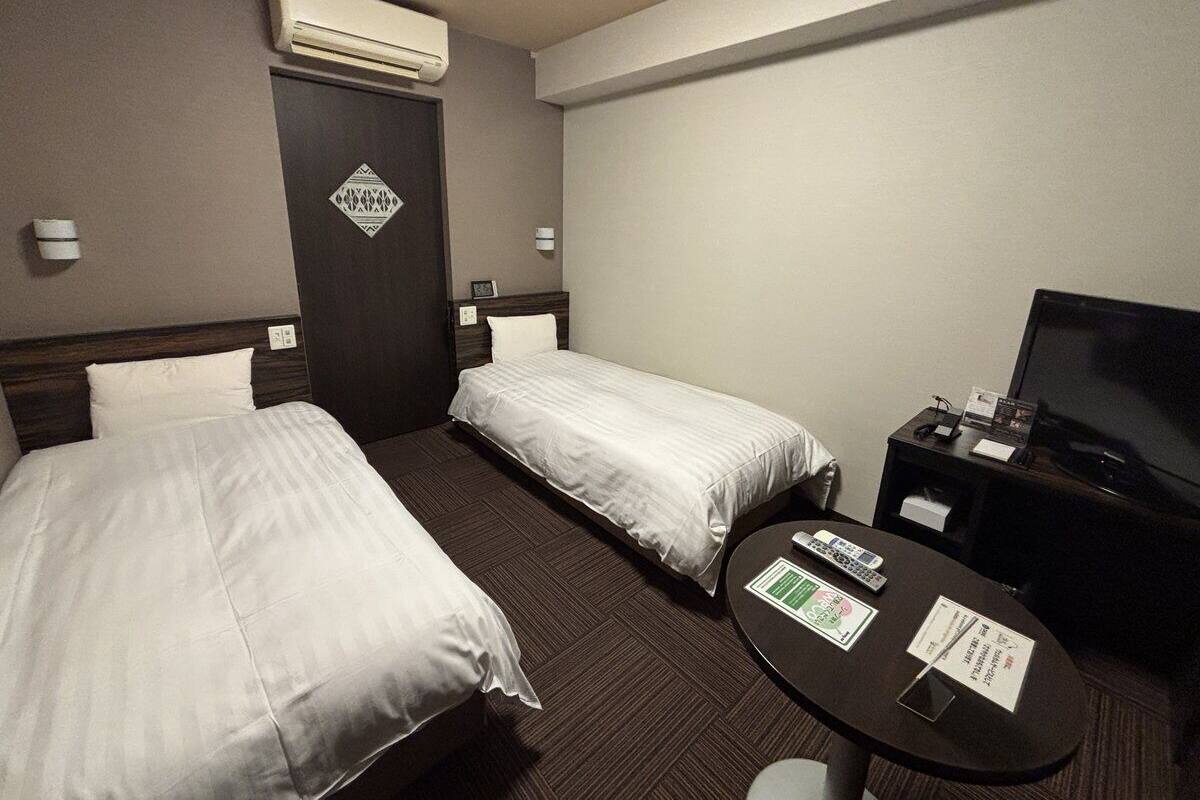 Habitación de hotel con dos camas, un televisor, una mesita y un equipo de aire acondicionado.