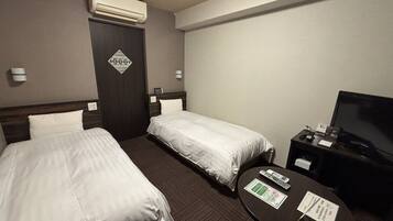 Quarto de hotel com duas camas, televisão, uma mesa pequena e ar condicionado.
