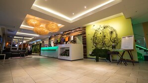 A modern hotel lobby with a reception desk, seating area, and a large decorative wall.