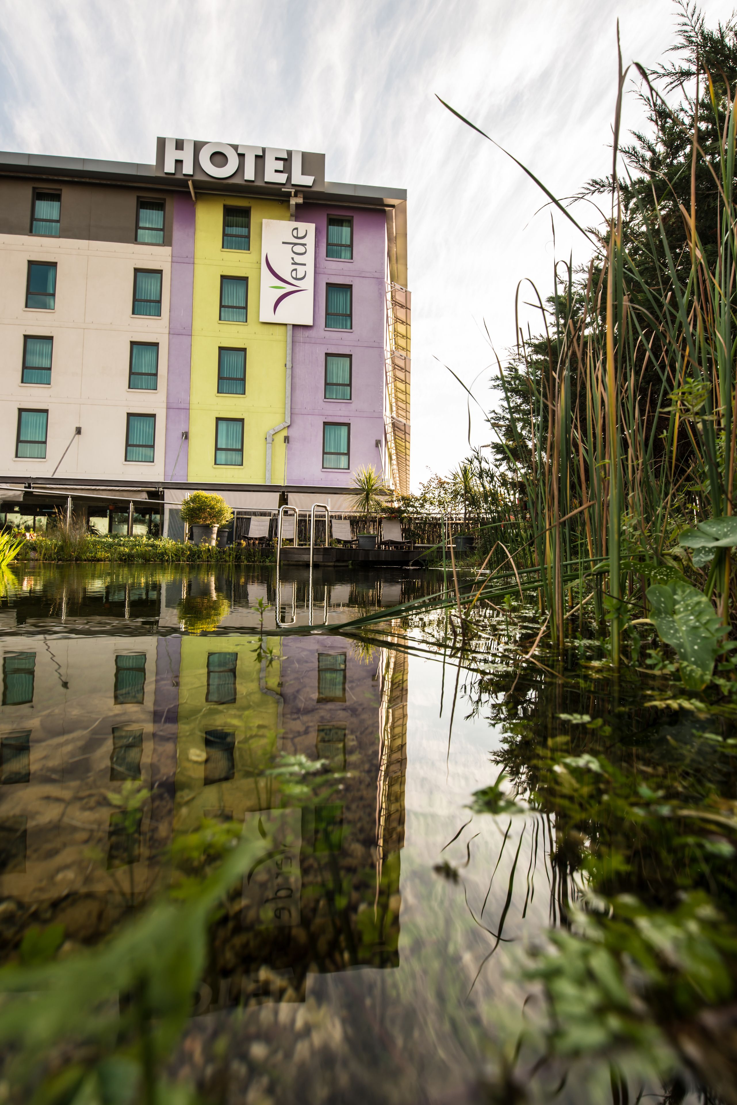 A hotel with a 'HOTEL' sign, a 'Verde' logo, and a reflection in a water body.