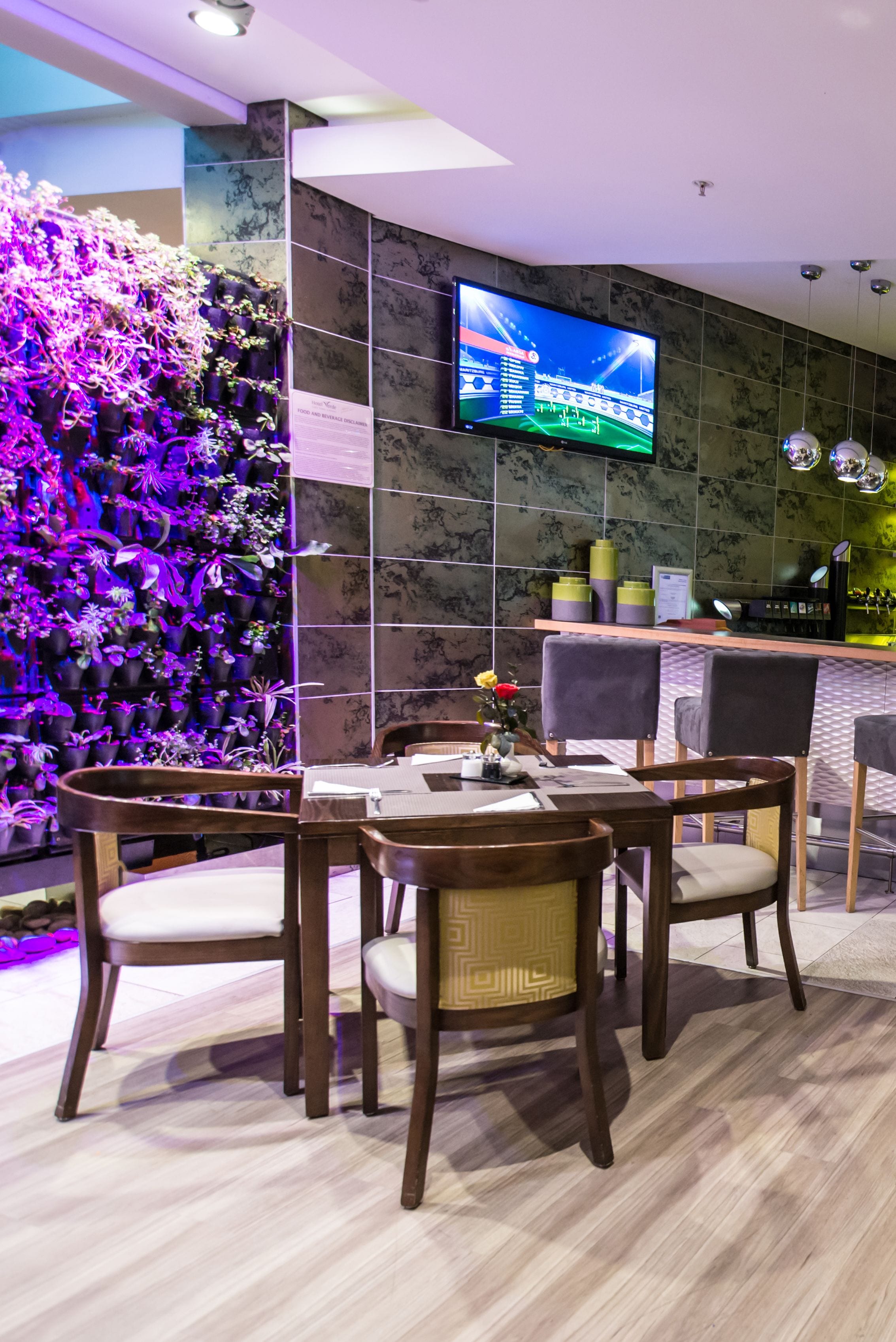 Un restaurante moderno con una pared de plantas en macetas, un televisor de pantalla plana y una zona de bar.
