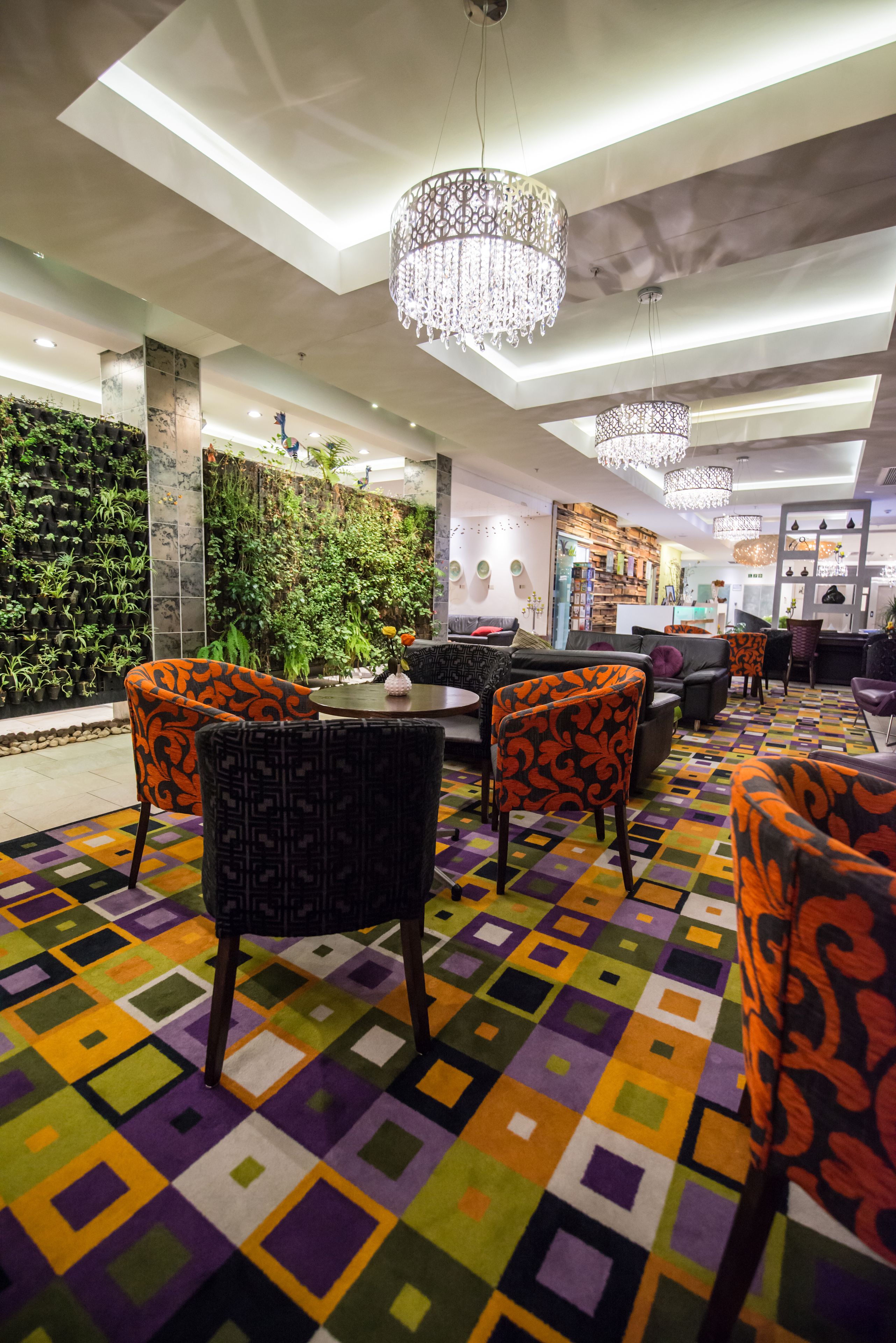Un interior moderno con una alfombra geométrica colorida, sillas con estampado naranja y una pared verde con plantas.