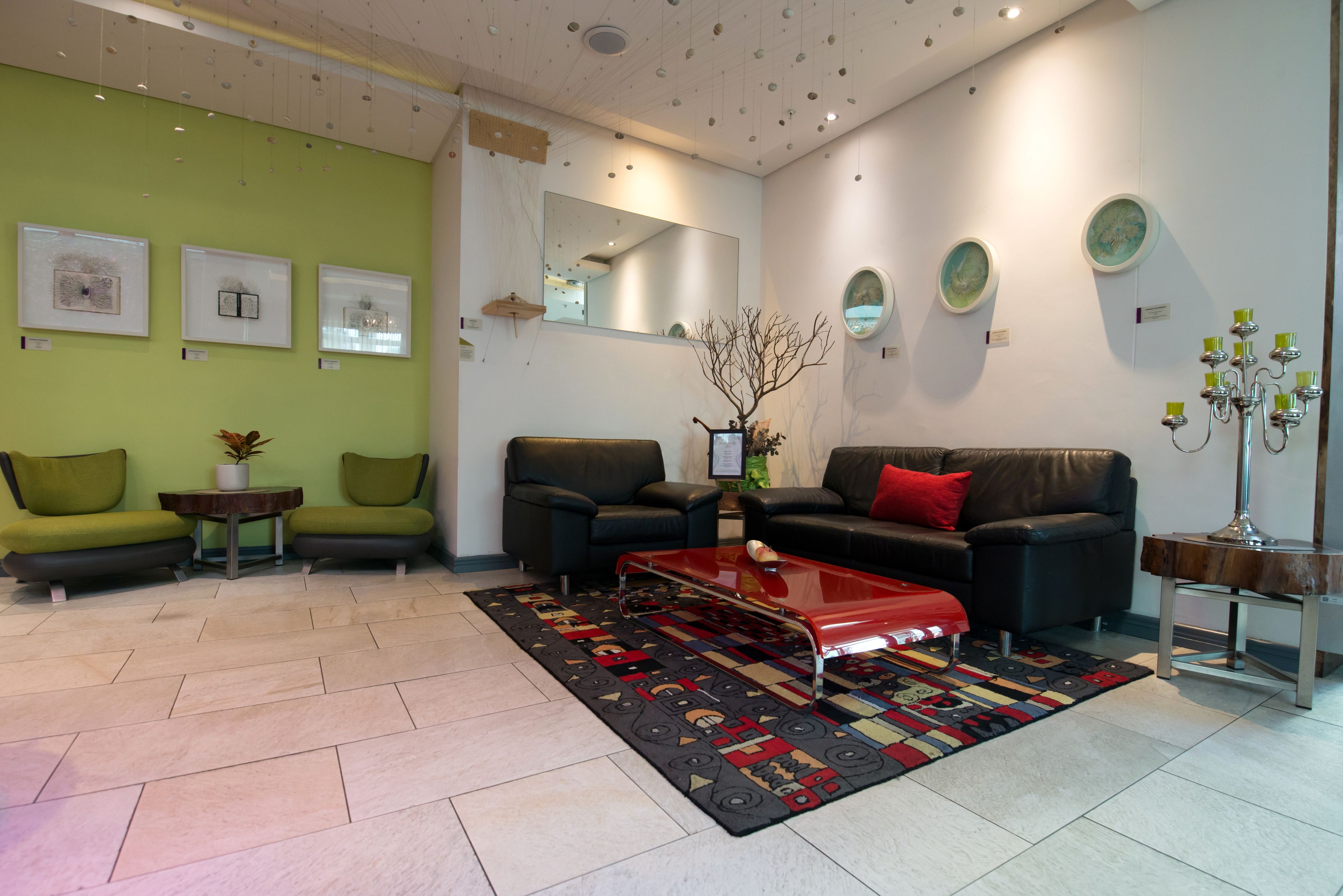 A modern living room with green walls, a black leather sofa, a red coffee table, and a patterned rug.