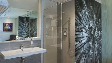Ein modernes Badezimmer mit Duschkabine aus Glas, einem großen Spiegel und einem Waschbecken mit Handtuchhalter.