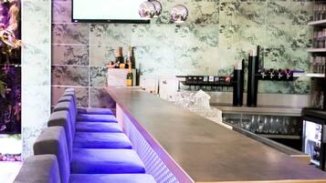A modern bar area with a long counter, cushioned seating, and a flat-screen TV mounted on the wall.