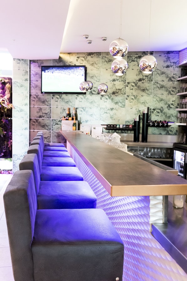 A modern bar area with a long counter, cushioned seating, and a flat-screen TV mounted on the wall.