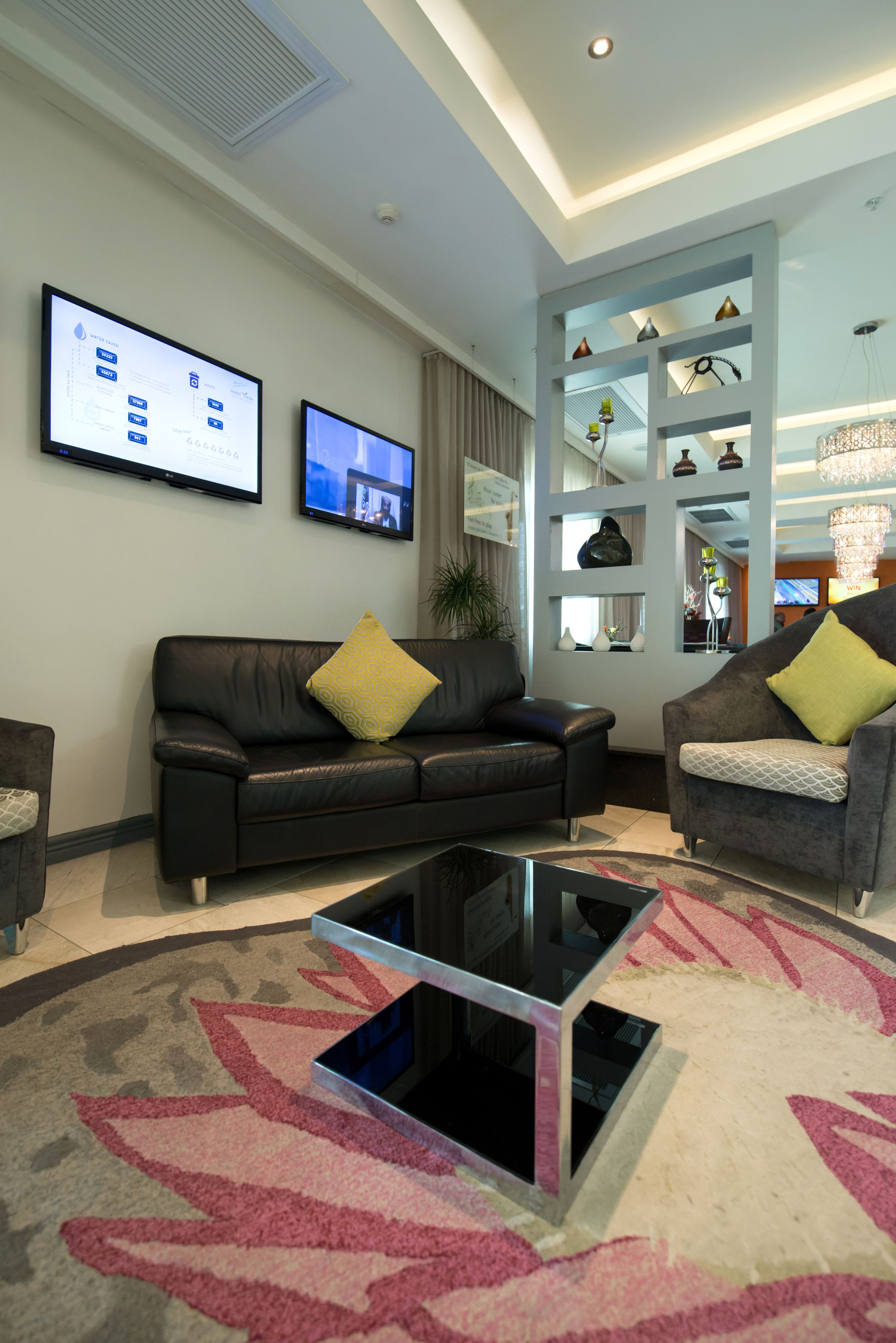 A modern living room with a black leather sofa, a grey armchair, and a glass coffee table.