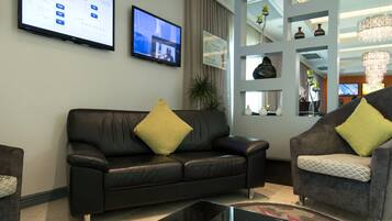 A modern living room with a black leather sofa, a grey armchair, and a glass coffee table.