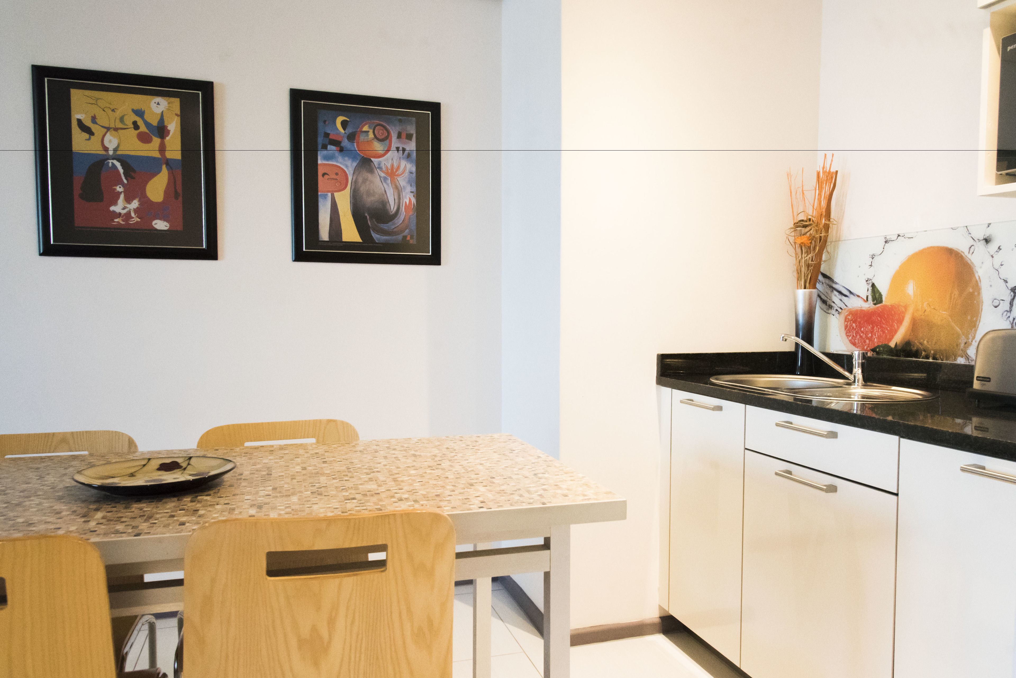 Een moderne keuken met een eettafel, stoelen en twee abstracte schilderijen in lijsten aan de muur.