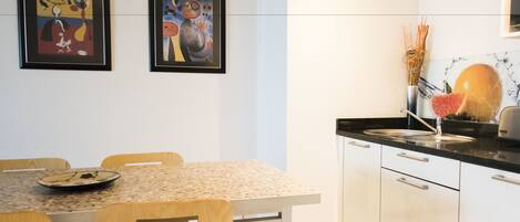 Een moderne keuken met een eettafel, stoelen en twee abstracte schilderijen in lijsten aan de muur.