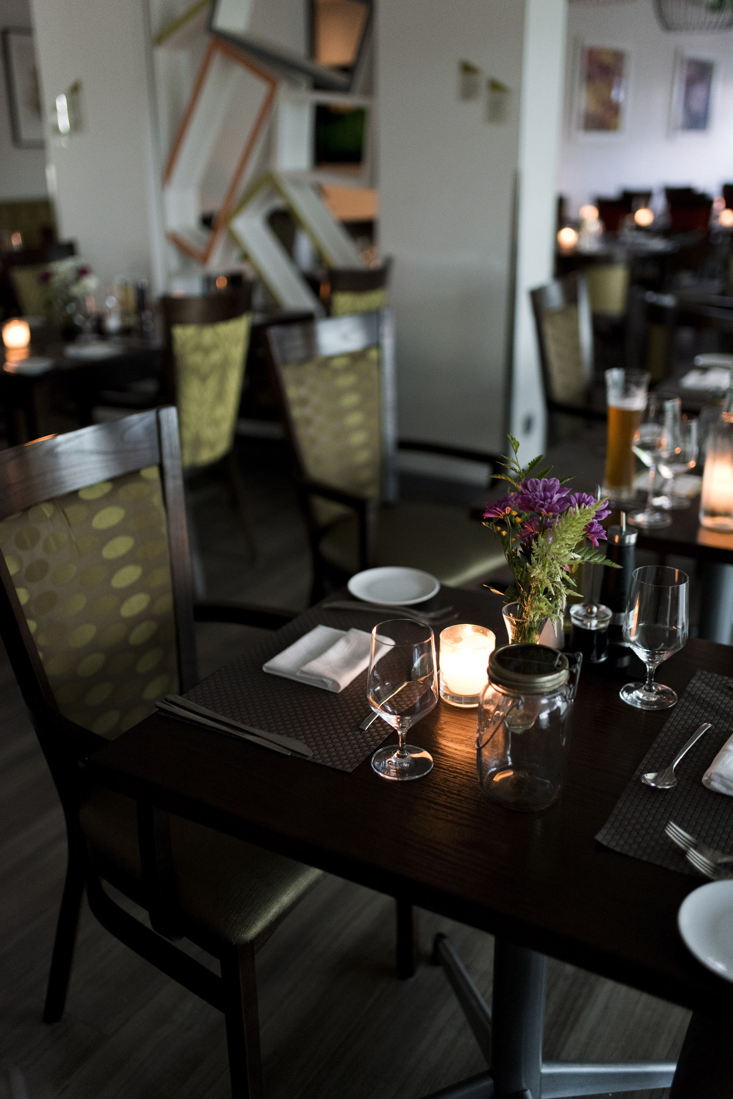 A dining table set with plates, glasses, a candle, and a vase with flowers.