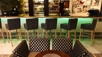 A bar area with a seating arrangement of five chairs and a sofa, a round wooden table, and a patterned wall with framed pictures.