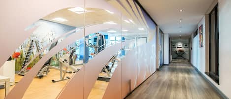 A modern gym with exercise equipment, a wooden floor, and a glass wall reflecting the interior.