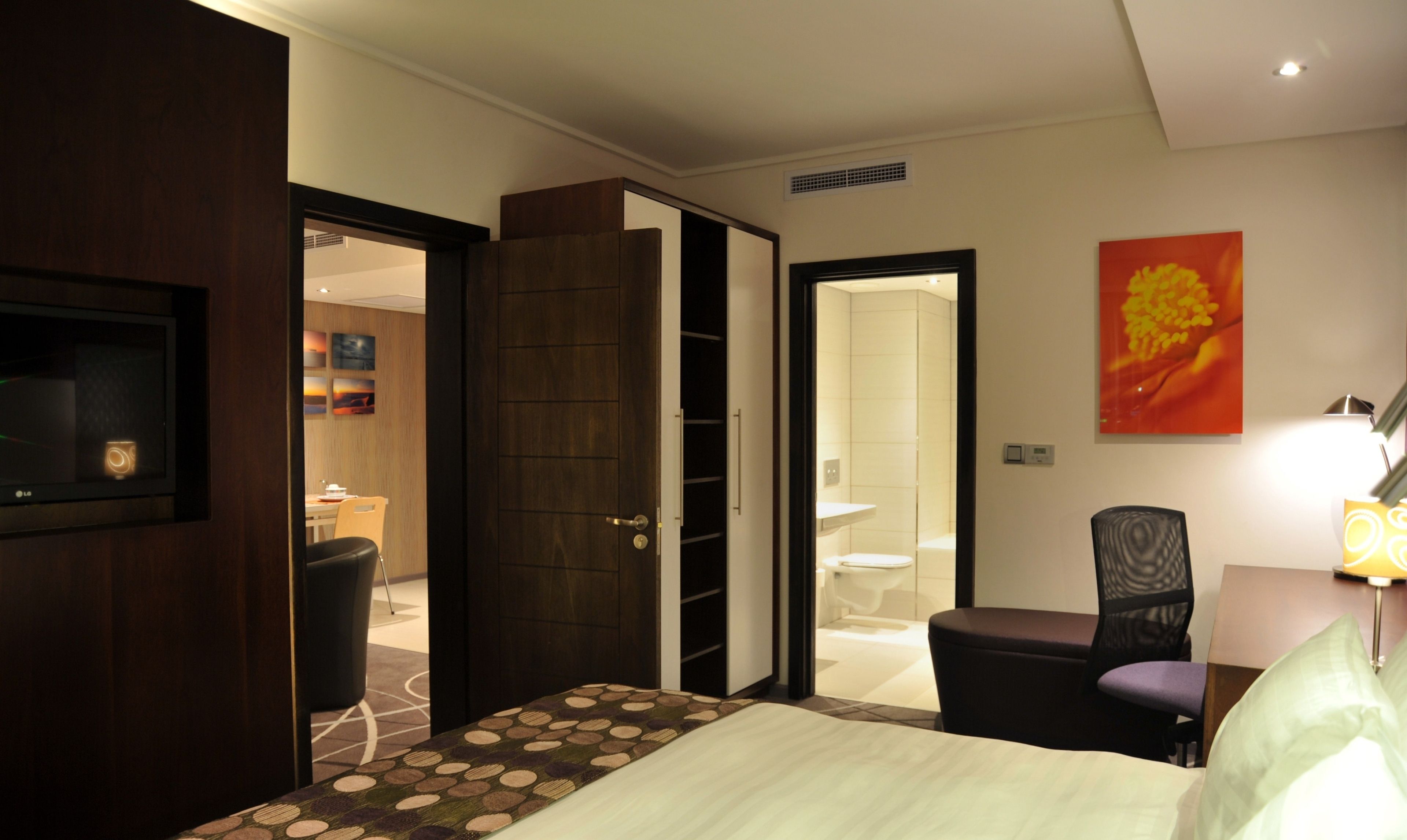 A hotel room with a bed, a desk, a chair, a TV, a bathroom, and a door leading to another room.