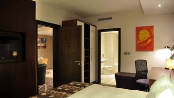 A hotel room with a bed, a desk, a chair, a TV, a bathroom, and a door leading to another room.