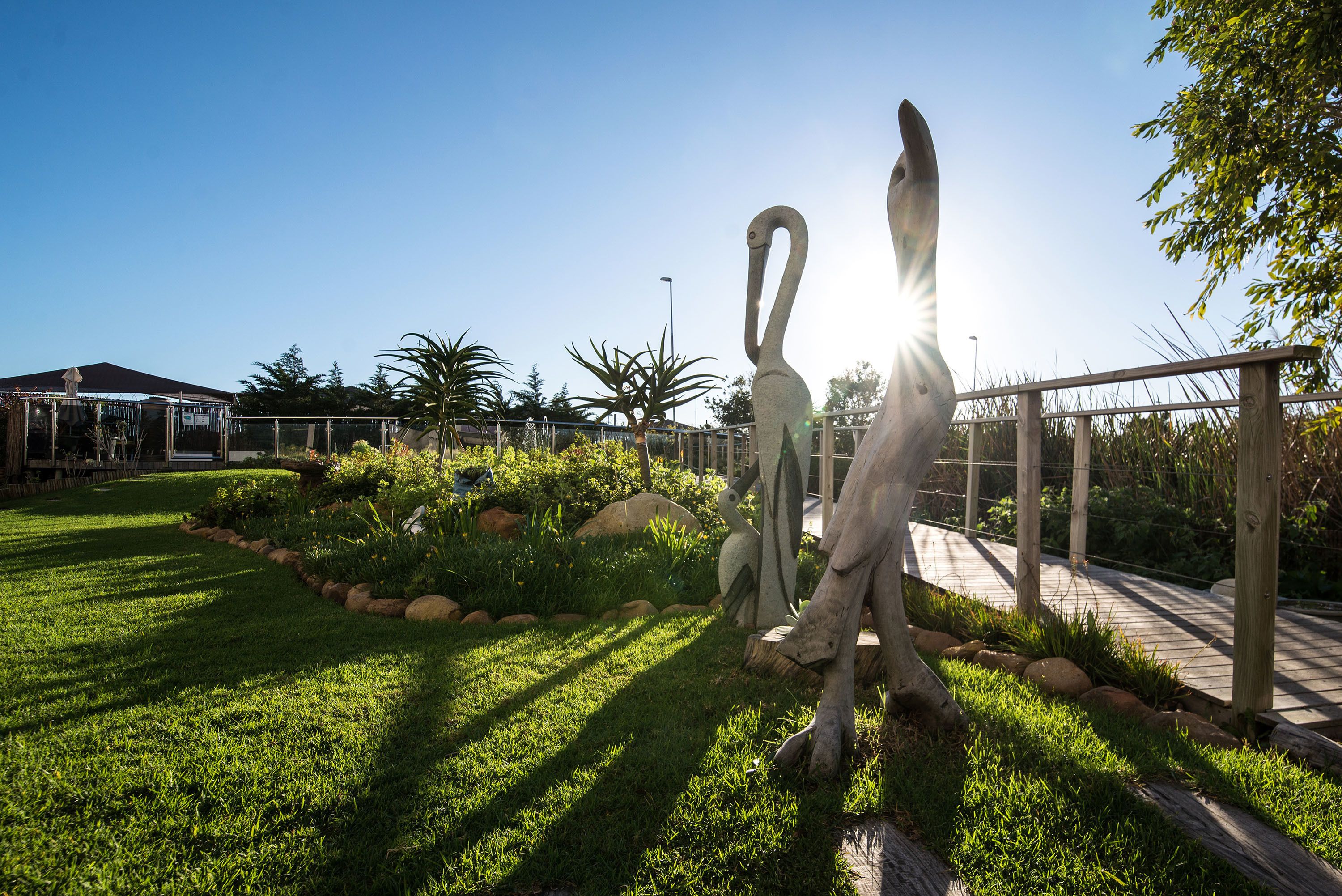A garden with a wooden fence, a metal sculpture, and a building in the background.