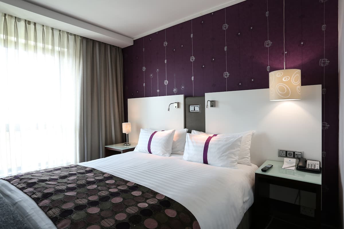 Une chambre d’hôtel comprenant un lit, une table de chevet, une lampe, un téléphone et un luminaire fixé au mur.