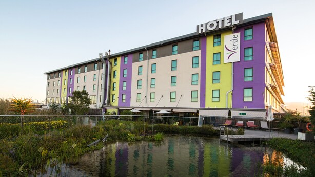 A multi-story hotel with a 'HOTEL' sign, a swimming pool, and a garden area with various plants.