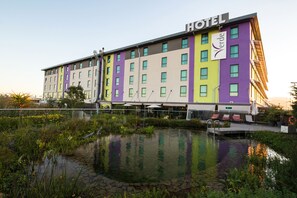 Ein mehrstöckiges Hotel mit einem 'HOTEL'-Schild, einem Schwimmbad und einem Garten mit verschiedenen Pflanzen.