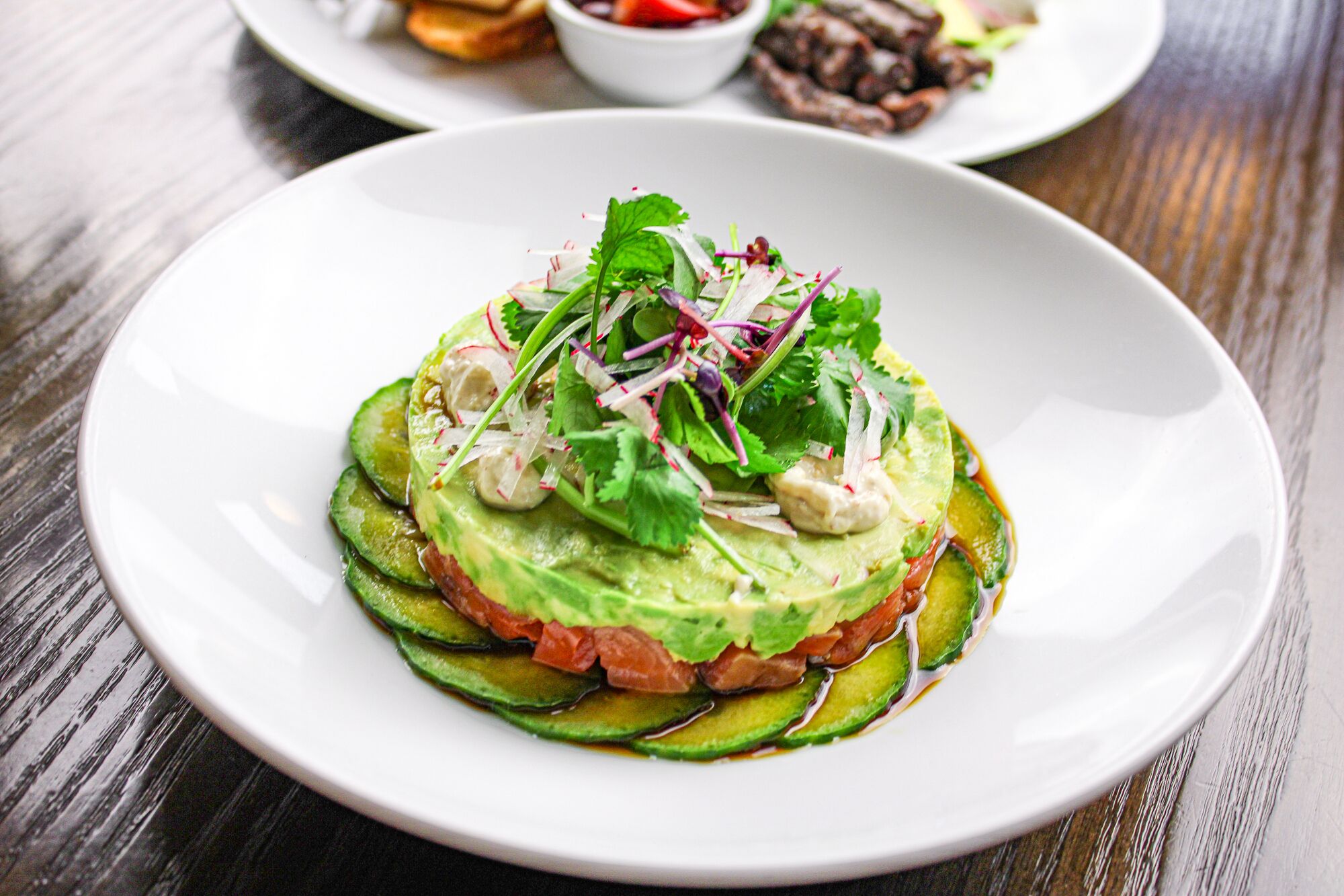 A plate of food with avocado, tomato, and cucumber slices, garnished with herbs.