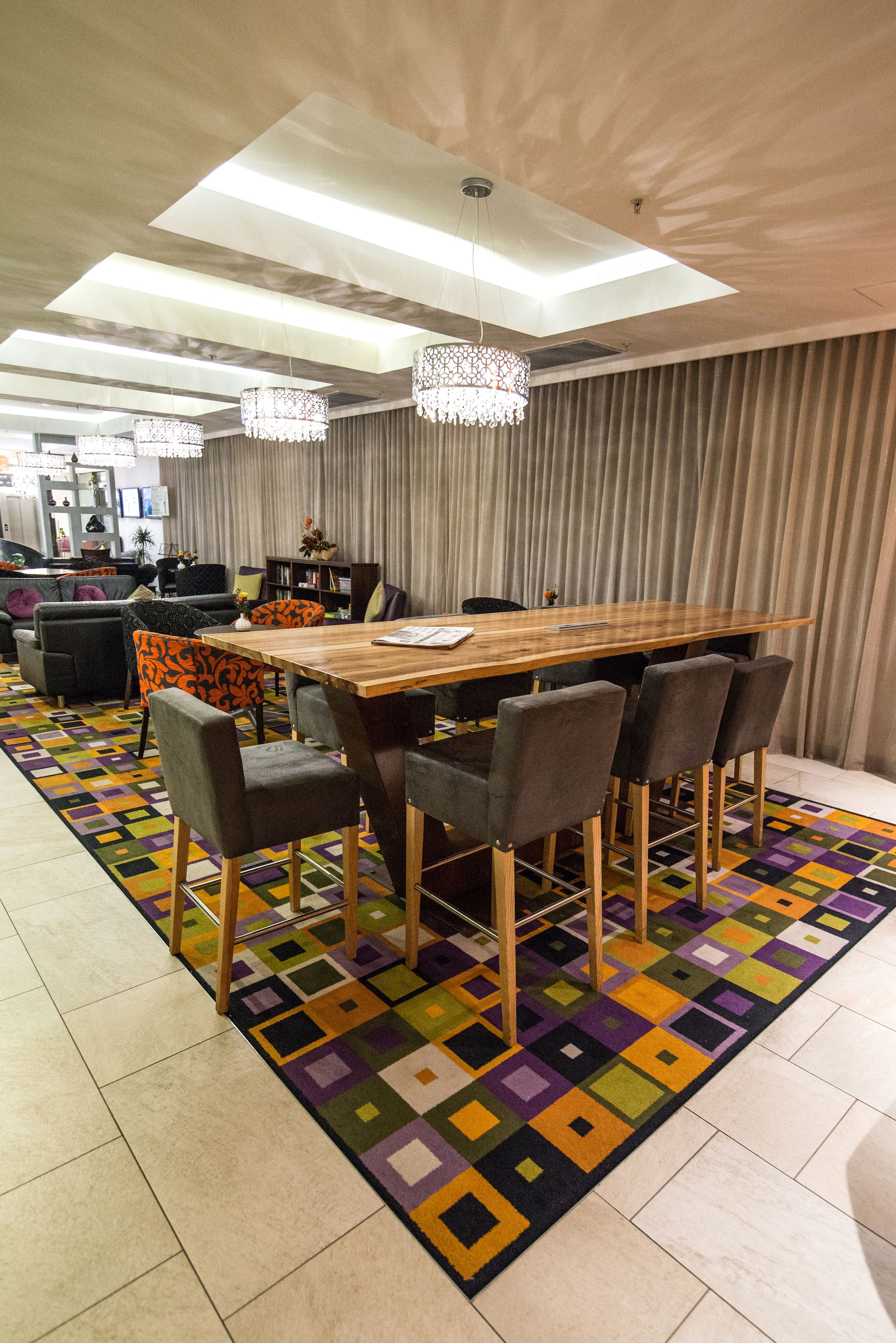 A dining area with a wooden table and chairs, a colorful rug, and a ceiling light fixture.