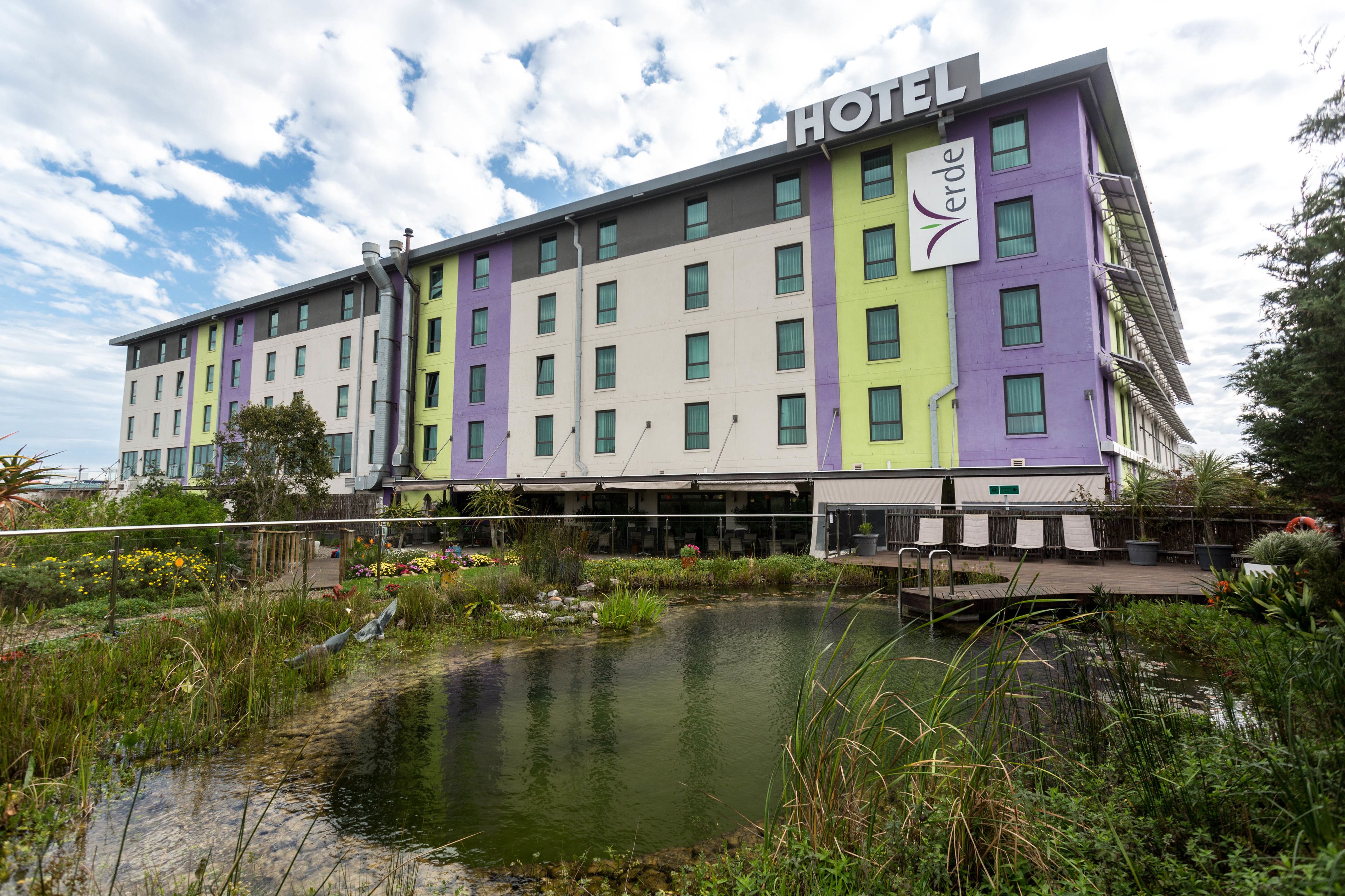 Een hotel met een meerlaags gebouw, een terras op het dak en een vijver op de voorgrond.
