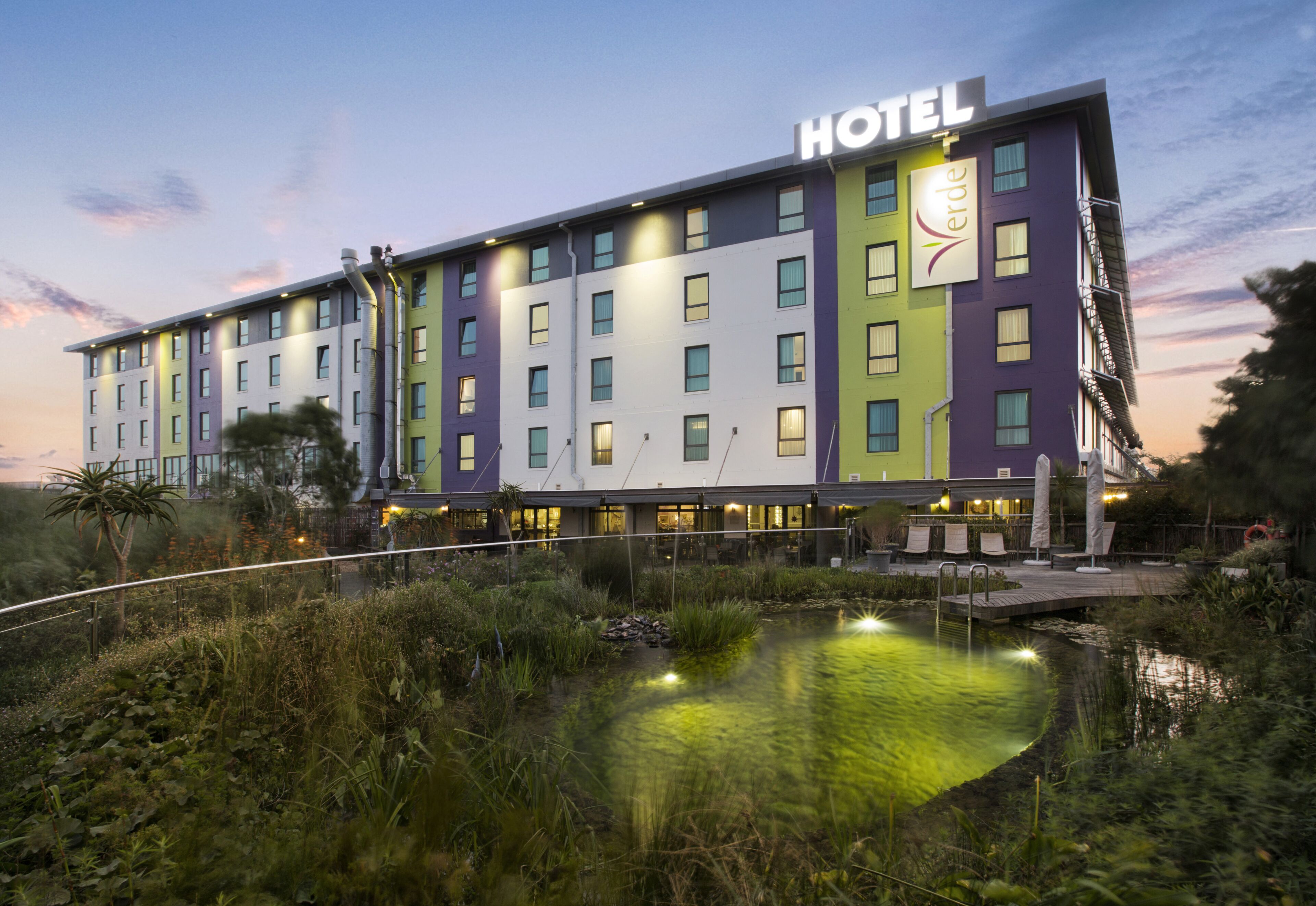 Un hotel de varios pisos con un letrero que dice "HOTEL Verde" y un reflejo en una fuente.