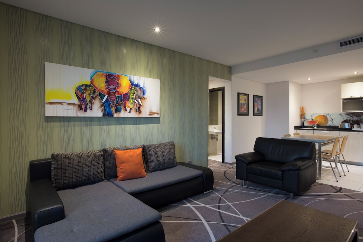 Un salon moderne avec un canapé d’angle, un fauteuil noir et un coin repas comprenant une table et des chaises.
