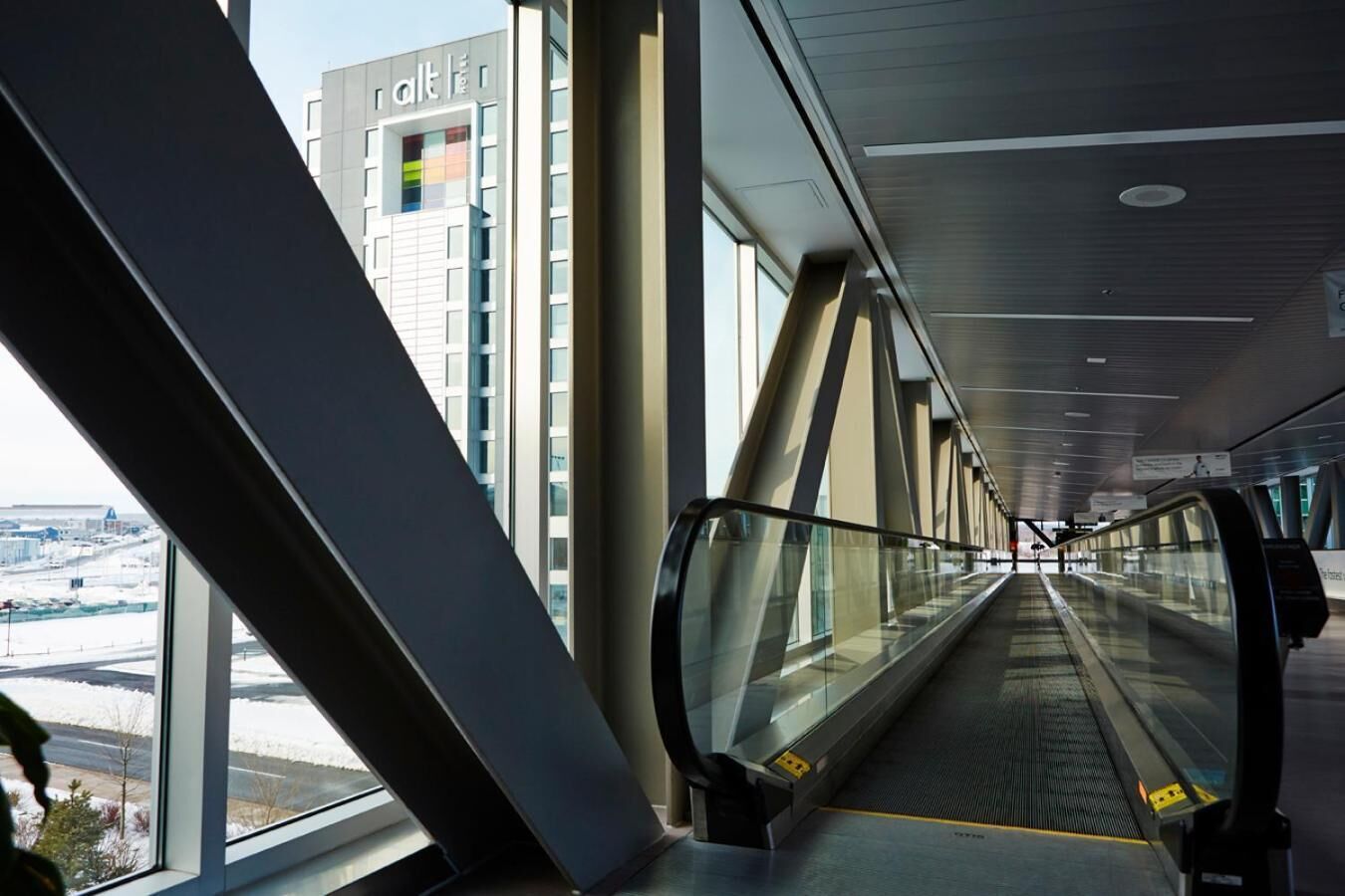 An indoor escalator in a modern building with large windows and a view of a cityscape.