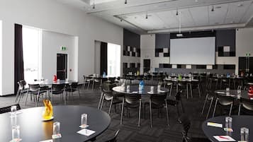 Un salón de conferencias con varias mesas redondas, sillas negras y una pantalla grande al frente.