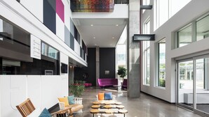 A spacious lobby with seating areas, a reception desk, and large windows providing natural light. - Alt Hotel Halifax Airport - In Terminal (Goffs)