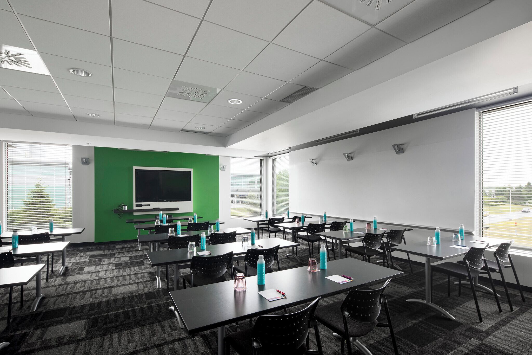 A conference room with tables, chairs, a projector screen, and a large window.