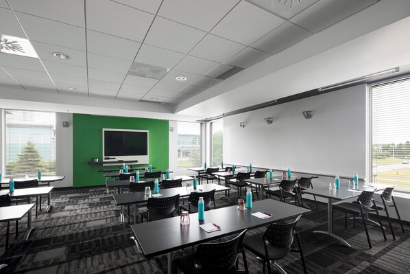 A conference room with tables, chairs, a projector screen, and a large window.