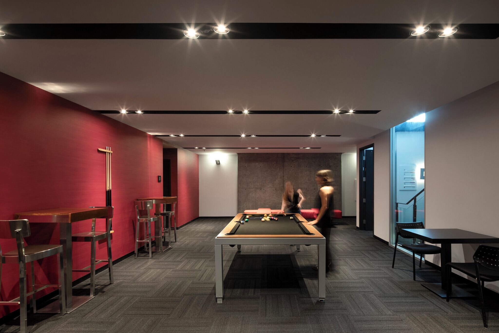 Une table de billard moderne, installée à l’intérieur, avec un mur rouge et un coin bar d’un côté.